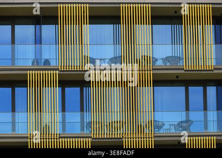 Modernes Apartmentgebäude mit sich wiederholenden Balkonen mit Glasgeländern und vertikalen architektonischen Elementen, die eine auffällige geometrische Fassade mit hohem Glanz schaffen Stockfoto