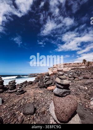 Ausgewogene steinhügel an einem felsigen vulkanischen Strand mit Meereswellen im Hintergrund an Playa del Duque Norte in Adeje, Teneriffa. Konzept des Gleichgewichts, ha Stockfoto