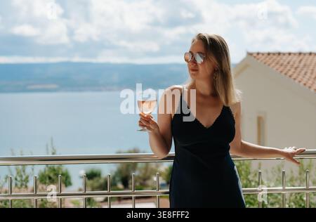 Frau genießt Rosenwein auf dem Balkon am Meer. Stockfoto