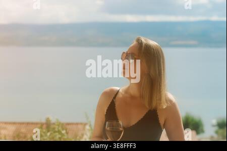 Frau genießt Rosenwein auf dem Balkon am Meer. Stockfoto