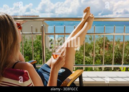 Frau entspannt sich auf der sonnigen Terrasse mit Wein. Stockfoto
