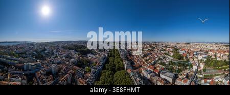 Aus der Vogelperspektive auf das weitläufige Stadtbild mit roten Ziegeldächern, die von Bäumen gesäumte Avenida da Liberdade und den Tejo unter einer hellen Sonne in Lissabon, Stockfoto