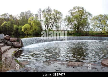 Ein künstlicher Wasserfall in einem Stadtpark. Eine Wasserkaskade mit Stufen im Stausee in der Nähe des Staudamms. Die Schönheit der Natur. Industrielle Architektur von Stockfoto