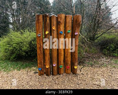 Rustikale Holz-Kletterwand mit bunten Griffen im Park. Konzept für Outdoor-Aktivität, Fitness und Kinderentwicklung in natürlicher Umgebung. Stockfoto