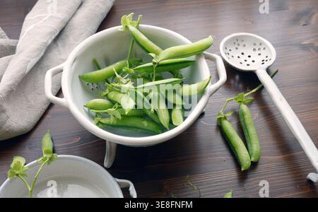 Frische grüne Bio-Erbsen in Keramikschalen auf dunklem Holztisch mit Kopierraum. Bei der Hochwinkelaufnahme werden junge Erbsenschoten und schalierte Erbsen hervorgehoben Stockfoto