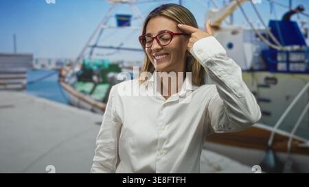 Die Frau zeigt mit dem Finger auf den Tempel am Straßenpier mit vertäuten Booten und Dock, trägt rote Brille und weißes Hemd; durchdachte Idee. Stockfoto