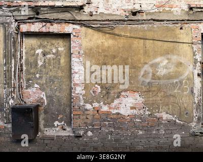 Alte zerstörte Mauer eines verlassenen Ziegelgebäudes mit Metallkästen und Kabeln Stockfoto