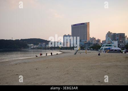 Die Menschen versammeln sich am Strand von Ilsan, während sich hinter dem Sand in Ulsan Hoteltürme, Geschäftsgebäude und der Strandpavillon erheben. Stockfoto