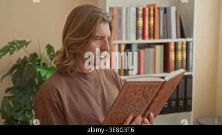 Mann, der ein reich verziertes Hardcover-Buch mit Fingern auf Seiten hält, steht und liest in einem mit Bücherregalen und Ordnern gesäumten Arbeitszimmer; Besinnung. Stockfoto