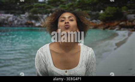 Frau mit freiliegendem Schlüsselbein, knirschende Lippen und kreuzende Zeigefinger im Studio an einem türkisfarbenen Küstenufer, direkt in die Kamera blickend; Trotz. Stockfoto