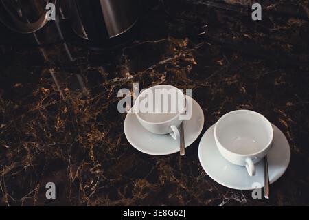 Zwei Tassen mit Löffel auf Marmortisch. Zwei weiße Kaffeetassen mit Kopierraum. Hotelservice. Heiße Getränke am Morgen. Sauberes Besteckkonzept. Stockfoto