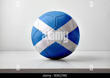 Ein Fußball mit der schottischen Flagge, das ein blau-weißes Kreuzmuster zeigt und zentral auf einem neutralen Hintergrund mit gleichmäßigem Studiolicht platziert ist Stockfoto