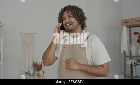 Mann, der das Smartphone am Ohr hält, Hand auf der Brust im Studio-Blumenladen trägt eine Schürze und spricht am Telefon; ruhiger Service. Stockfoto
