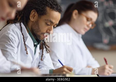 Biracial männlicher Medizinstudent schreibt Notizen während des Wissenschaftsunterrichts Stockfoto