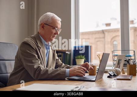 Senior männlicher Professor, der im Büro an Laptop arbeitet Stockfoto
