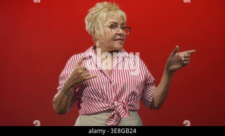 Die ranghöchste hispanische Frau zeigt mit dem Finger und macht Handgeste, die Hand und Lächeln in einem Studio zeigt; freudige Verbindung. Stockfoto