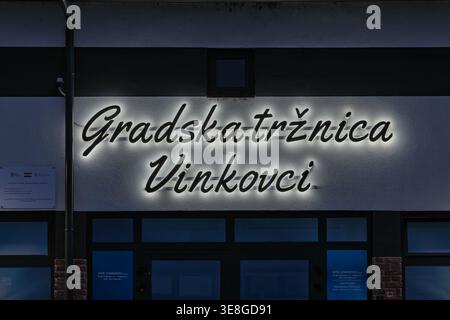 Vinkovci, Kroatien - 22. März 2026: Beleuchteter Stadtmarkt Vinkovci Neonschild, bei Nacht an einer Fassade des Marktgebäudes angebracht, mit einem Stadtarchitekten Stockfoto