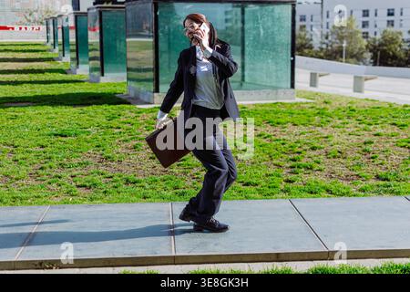 Geschäftsfrau, die draußen läuft und am Telefon mit Aktentasche spricht Stockfoto