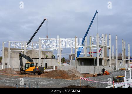 Krane und Arbeiter montieren Stahlträger auf Betonkonstruktionen auf der aktiven Baustelle mit Maschinen Stockfoto