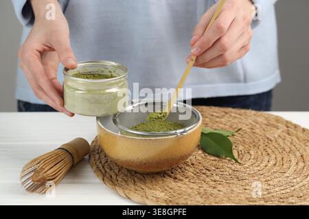 Frau, die Matcha-Pulver in eine Schüssel am weißen Holztisch siebt, Nahaufnahme Stockfoto