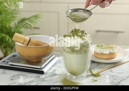 Frau, die Matcha-Pulver auf Drink gesiebt hat, an weißem Marmortisch, Nahaufnahme Stockfoto