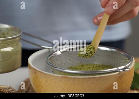 Frau, die Matcha-Pulver in eine Schüssel am weißen Tisch siebt, Nahaufnahme Stockfoto