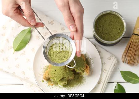 Frau siebt Matcha-Pulver auf Croissant an weißem Holztisch, Blick von oben Stockfoto