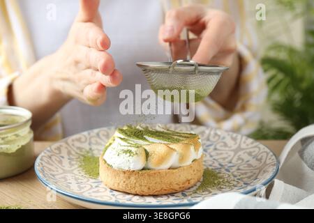 Frau siebt Matcha-Pulver auf Meringue-Tarte am Holztisch, Nahaufnahme Stockfoto