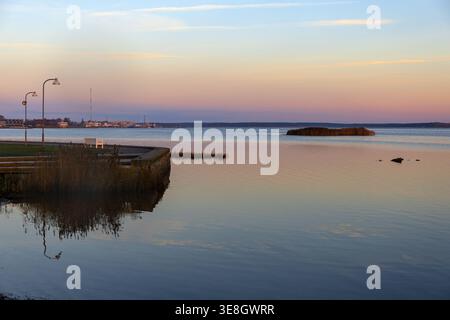 Ruhiger Blick auf das Meer bei Sonnenaufgang mit ruhigem Wasser und pastellfarbenem Himmel in Haapsalu, Estland. Ruhige Küstenlandschaft mit entfernter Küste und Kopierraum. Stockfoto
