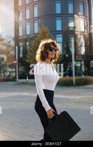 Lifestyle. Mode. Schöne Frau, die mit Handtasche läuft. Weibliches Model draußen in der Stadt. Stilvolles Outfit mit Sonnenbrille. Moderner Business Lifestyle. Stockfoto