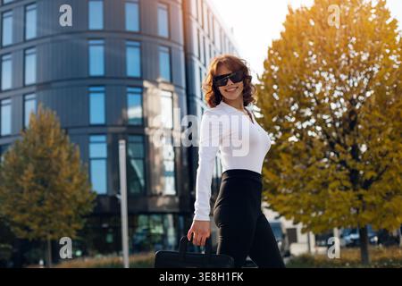 Lifestyle. Städtisch. Attraktive Frau, die mit Handtasche läuft. Weibliches Model draußen in der Stadt. Stilvolles Outfit und Sonnenbrille. Business Lifestyle Konzept. Stockfoto