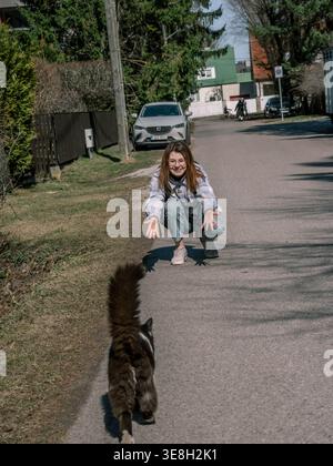 Junge Frau, die im Frühjahr eine flauschige Streunerkatze in Kristiine, Tallinn, Estland, ruft Stockfoto