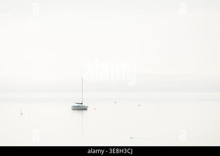 Ein einsames Segelboot in einer minimalistischen Meereslandschaft, das auf dem Firth of Forth im Nebel, Aberdour, Fife, Großbritannien, liegt. Stockfoto