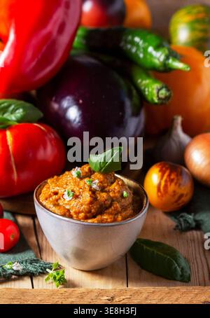 Auberginen-Kaviar in einem Glas und Gemüse auf hölzernem Hintergrund. Stockfoto