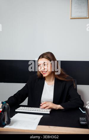 Frau, die am Schreibtisch mit Computertastatur arbeitet. Business-Arbeitsplatz und Corporate-Job-Konzept. Weibliche Profi lächelt und arbeitet in der modernen o Stockfoto