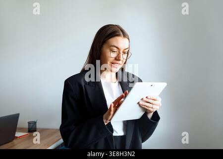 Frau, die ein Tablet am Schreibtisch benutzt. Schöne Geschäftsfrau, die mit digitalem Workflow arbeitet. Weibliche Profi, die Technologie in modernen Unternehmensumgebungen einsetzen Stockfoto