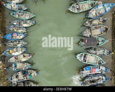 Aus der Vogelperspektive sehen Sie farbenfrohe Boote, die sich eng auf dem Jepara Floating Fish Market gruppieren, deren pulsierende Rümpfe im Kontrast zum trüben grünen Wasser Jepara stehen Stockfoto