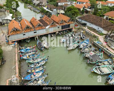 Aus der Vogelperspektive auf dem Jepara Floating Fish Market, einer lebhaften Szene, in der rustikale Schiffe auf die Erdtöne der gekachelten Dächer treffen, Stockfoto