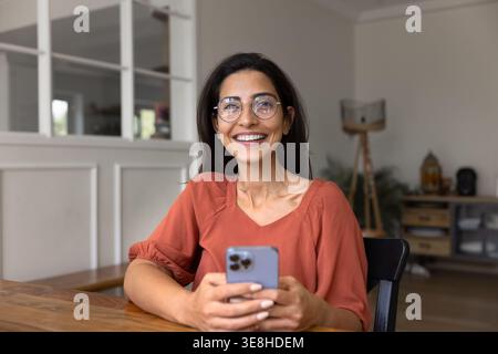 Porträt einer glücklichen brasilianischen Frau, die mit dem Smartphone am Schreibtisch sitzt Stockfoto