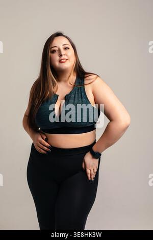 Körperpositivitätskonzept. Schöne, lächelnde Frau in großer Größe mit voll kurvigem Körper posiert in Studiosportbekleidung. Attraktives weibliches Modell drückt selbst-werteliste aus Stockfoto