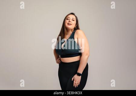 Aufbauabnahmekonzept. Attraktive Frau in Übergröße mit Kurven und sportlicher Körperhaltung posiert anmutig in Studiosportbekleidung. Weibliches Modell hebt i hervor Stockfoto