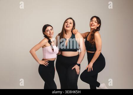 Aufbauabnahmekonzept. Fröhliche Fitness-Freundinnen mit kurvigem Model in Plus Größe lachen zusammen in Studio-Sportbekleidung. Verschiedene weibliche Gruppen Stockfoto