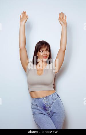 Eine Frau steht mit hochgezogenen Armen in fröhlicher Pose, lächelt breit und trägt ein lässiges Outfit. Sie hat Spaß und drückt Glück in einem bri aus Stockfoto