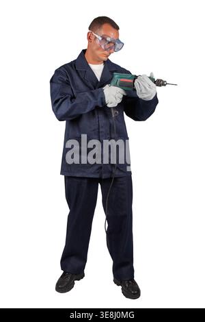 Ein Mann mit marineblauer Arbeitsuniform, Schutzbrille und Handschuhen steht vor einem weißen Hintergrund und hält eine kabelgebundene Bohrmaschine. Stockfoto