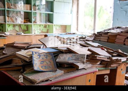 Ukraine, Pripyat, Tschernobyl-Ausschlusszone: Chaotische Anhäufungen von staubigen alten sowjetischen Lehrbüchern und Kinderbüchern auf Schreibtischen und auf dem Boden in heruntergekommenen elementaren en en Stockfoto