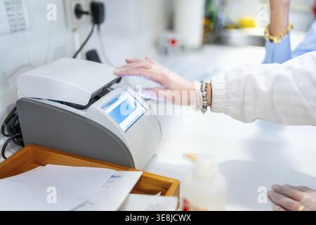 Apotheker Hand in einem weißen Handschuh, der ein professionelles medizinisches Gerät mit einem digitalen Bildschirm bedient und an Forschung und Entwicklung in einem modernen Labor arbeitet Stockfoto