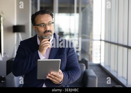 Geschäftsmann mittleren Alters, der einen digitalen Bericht auf einem Tablet liest Stockfoto