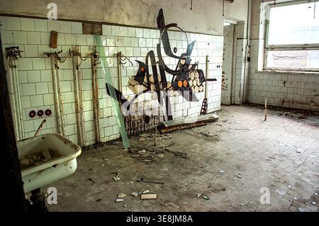 Verlassenes Badezimmer in der Pripyat-Schule Tschernobyl-Ausschlusszone Ukraine mit altem Waschbecken, gekachelten Wänden mit Graffiti, Glasscherben und Schutt auf dem Boden, Stockfoto