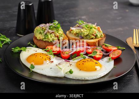 Ausgewogene gesunde Mahlzeit mit Spiegeleiern und Avocadotoast auf schwarzem Teller Stockfoto