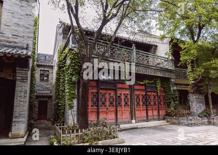 Traditionelles chinesisches Hofhaus mit roten Holztüren, Efeu-bedeckte Fassade und Bäumen entlang der Steinstraße in Gubei Town China Stockfoto
